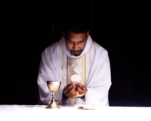 A priest is holding his hands in prayer.