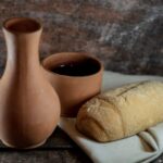 A loaf of bread and some wine in a vase