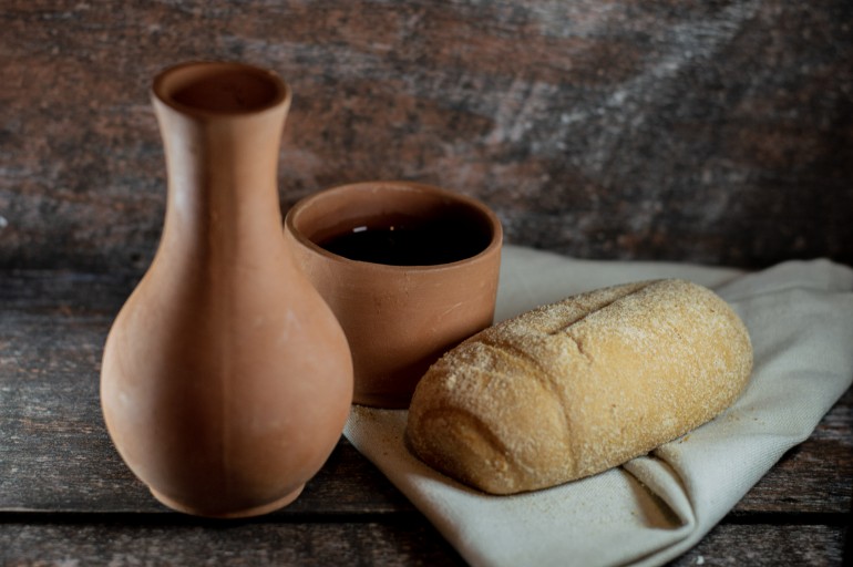 A loaf of bread and some wine in a vase