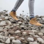 A person wearing boots and jeans on top of rocks.