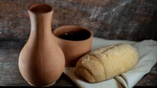 A loaf of bread and some wine in a vase