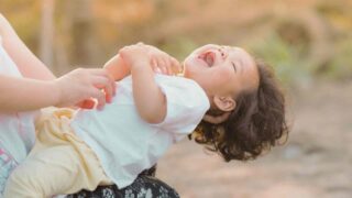 A little girl is laughing while being held by her mother.