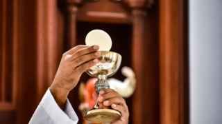 A person holding up a cup and a cross