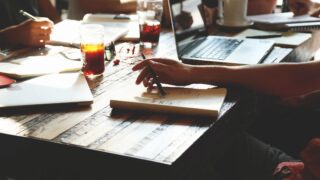 A person is writing on a notebook at a table.